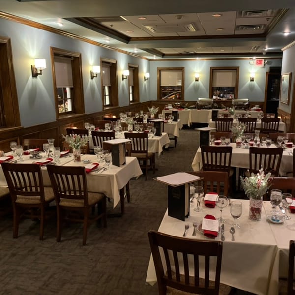 A restaurant dining room with set tables, white tablecloths, and warm lighting, ready for guests.