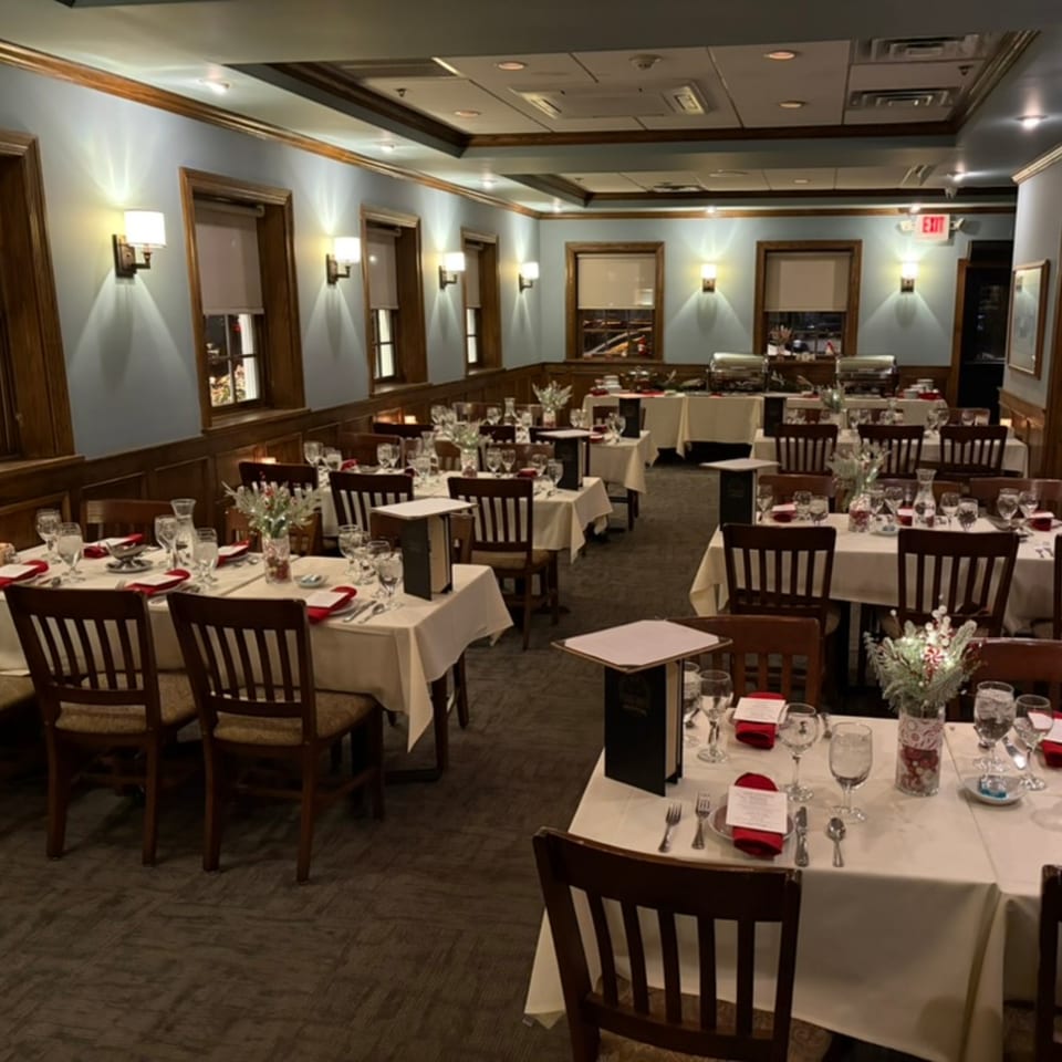 A restaurant dining room with set tables, white tablecloths, and warm lighting, ready for guests.