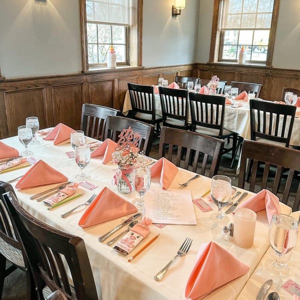 Tables set for a baby shower with pink napkins, centerpieces, and "It's a Girl" decorations.