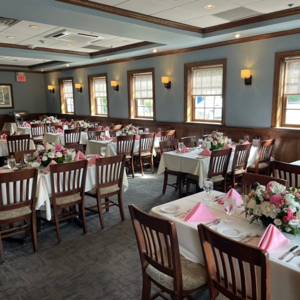 A dining room with multiple tables set with white tablecloths, pink napkins, and floral centerpieces.