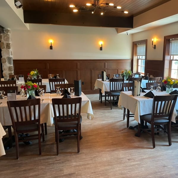 Elegant dining room with white-clothed tables, dark wooden chairs, and floral centerpieces under warm lighting.