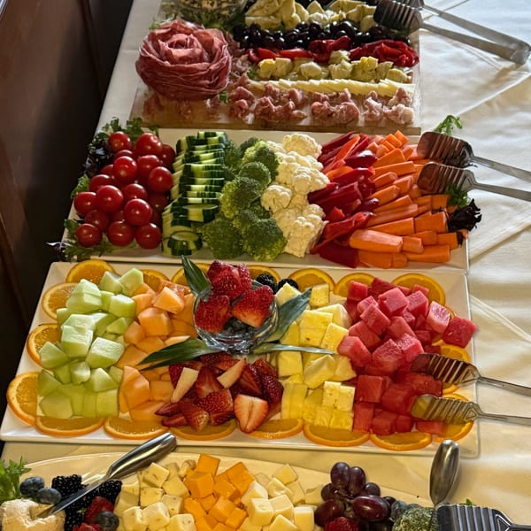 A buffet spread with charcuterie, vegetable crudités, fruit platters, and cheese boards.