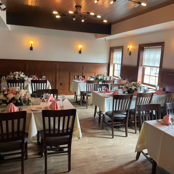Elegant dining room with white tablecloths, pink napkins, floral centerpieces, and dark wood chairs.