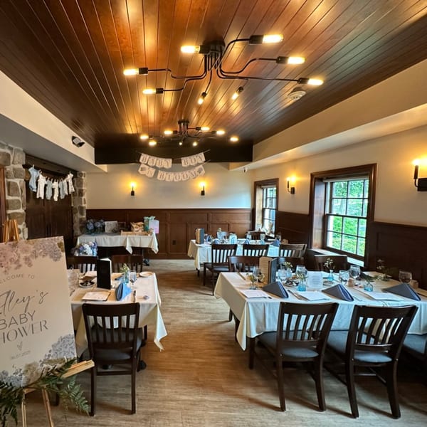 Restaurant dining room set up for a baby shower with tables, chairs, and "Baby Boy in Bloom" banner.