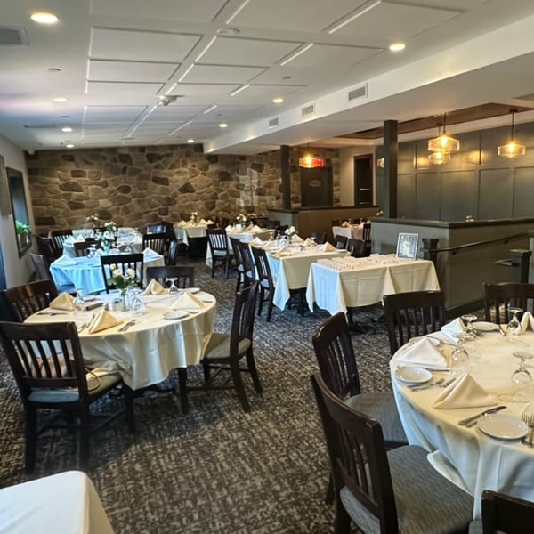 Elegant restaurant dining room with set tables, stone walls, and warm lighting.