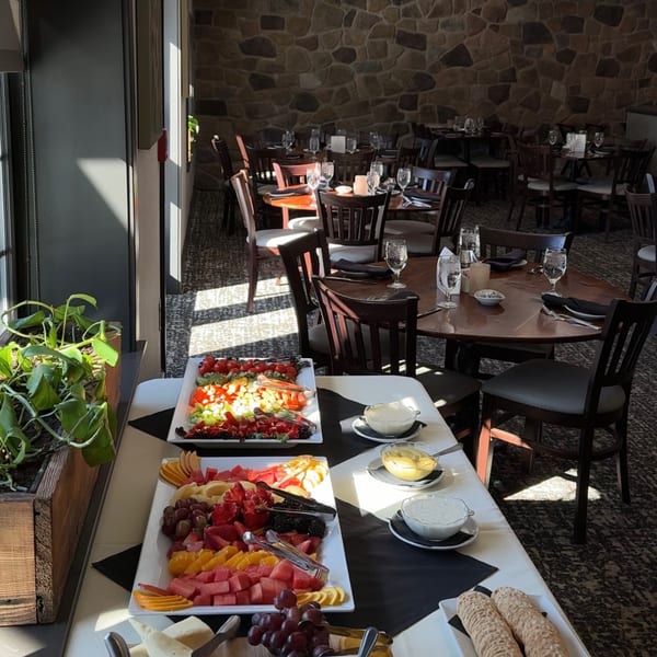 Buffet table with fruit and vegetable platters, dips, and crackers in a restaurant dining room.