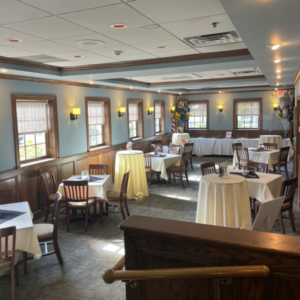 A restaurant dining room with light blue walls, wood paneling, and tables set for an event.