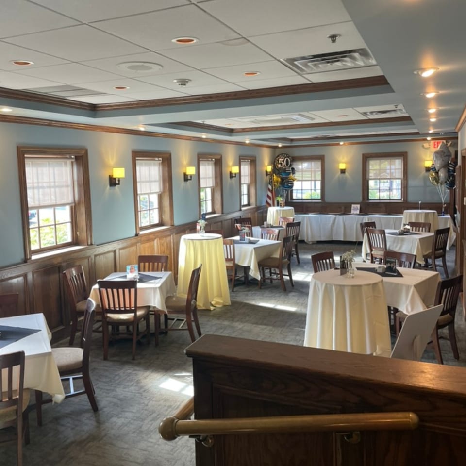 A restaurant dining room with light blue walls, wood paneling, and tables set for an event.