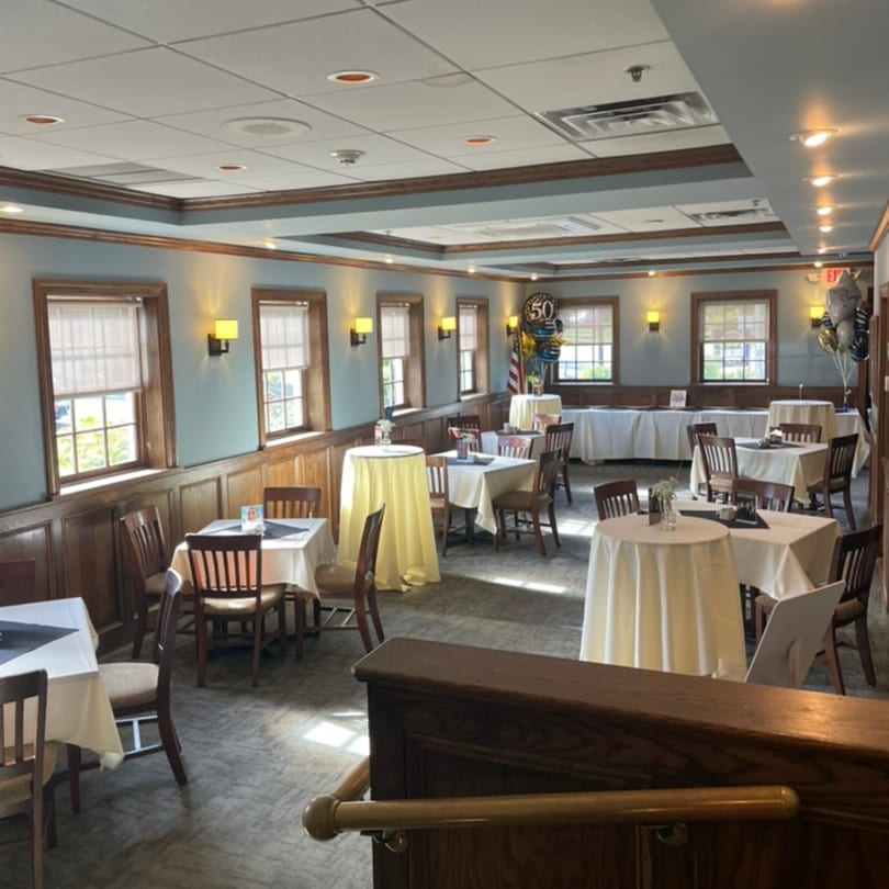 A restaurant dining room with light blue walls, wood paneling, and tables set for an event.