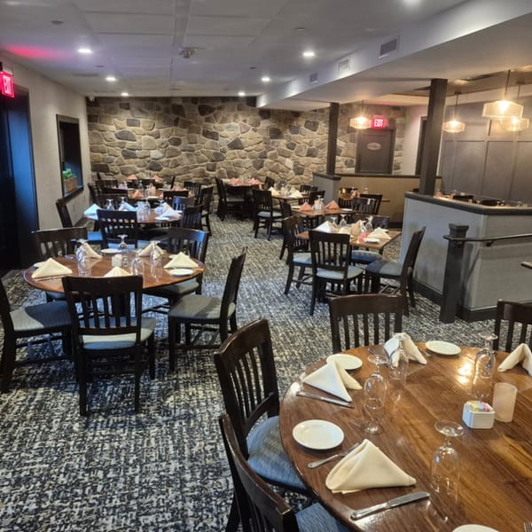 A dining room with many round wooden tables set with white napkins and glasses, and stone walls.